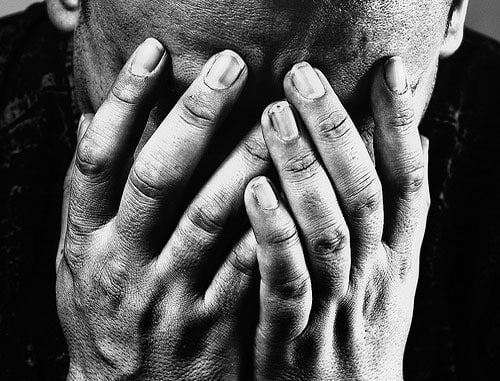 In a black and white photo, a person covers their face with their hands.